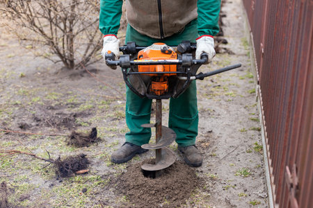 Gardener using tools hand-held soil hole drilling machine or portable manual earth auger for prepare the soil for planting shrubs.の写真素材