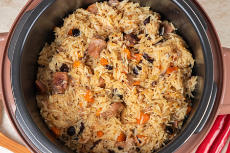 Pilaf with turkey, mutton, beef or pork, carrots, onions, garlic, pepper and raisin in the modern multicooker. A traditional dish of Asian cuisine. Top view. Close-up.の写真素材