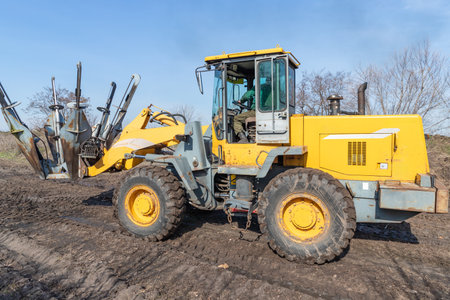 Male worker drives tree transplanter heavy machine. Landscaping, seasonal agricultural engineering, large trees landing machines. Planting of trees using tree spade - specialized machine for transplanting and transport trees.の写真素材