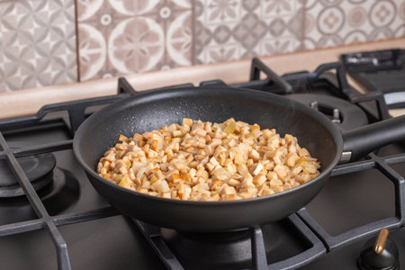 Frying mushrooms in a fry pan. Frying pan full of chopped, fresh bay boletes and boletus or king oyster mushrooms or eryngii (Pleurotus eryngii) during the process of frying. Gas stove in the background. Close-up.の写真素材