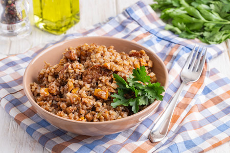 Buckwheat with meat and shrooms in a brown bowl on a light background. Russian buckwheat porridge with meat and vegetables on wooden table, rustic style. Close-up.の写真素材