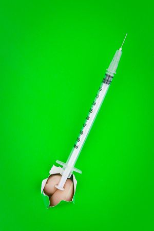 A person holding a long syringe through the hole in a green wall.の写真素材