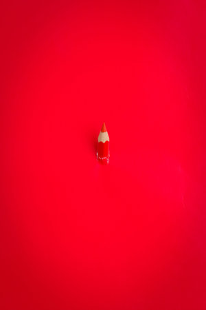Red colored pencil peeks through a solid red background.
