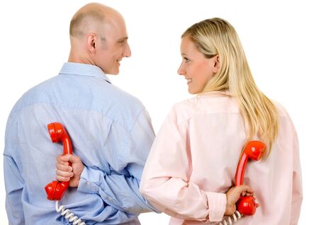 Rear view of happy young couple with red telephones behind back; white studio background.の写真素材