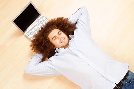 Man laying on the floor with his eyes closed with a laptop near his head.の写真素材