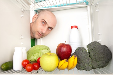 Portrait of young man looking at different healthy food inside refrigerator.の写真素材