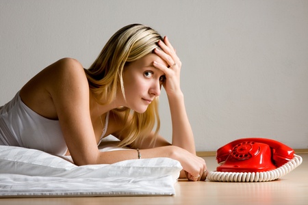 Side portrait of blond haired teenager lying next to red retro telephone, gray background.の写真素材