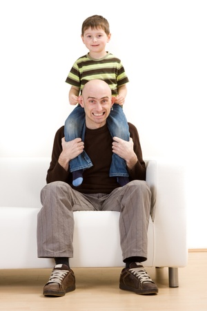 Happy young boy sat on fathers shoulders on sofa, white background.の写真素材
