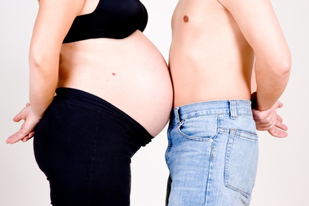 Side view of pregnant woman with bare stomach pressed against bare chested man, white background.
の写真素材