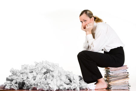 A woman sitting on a stack of files next to crumpled paper. の写真素材