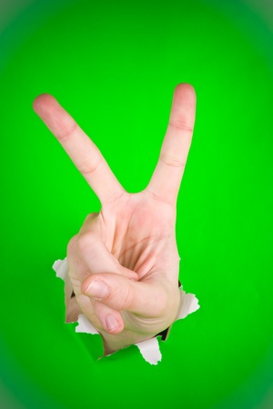 A victory sign made by a hand, ripping through a bright green paper.の写真素材
