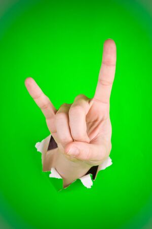 Hand sign of the horns coming through torn green paper.の写真素材