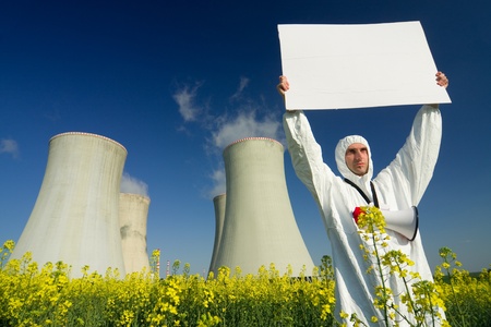 A view of a man in a protective suit, holding a blank sign in front of a nuclear power plant.の写真素材