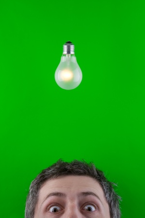 A view of the top half of a man's head underneath a traditional incandescent light bulb.  Bright green background.  Theme:  bright idea, innovation の写真素材