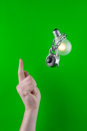Human pointing a finger towards a locked electric bulb, on green background.の写真素材
