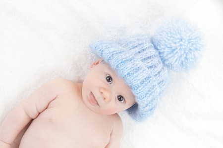 Closeup of cute male baby lying in bed or cot with blue woolly hatの写真素材