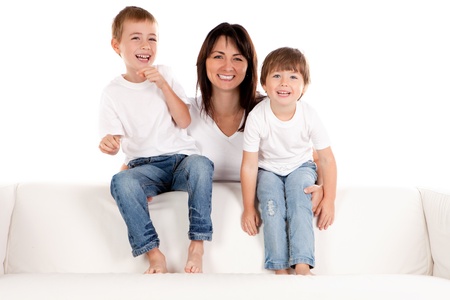 A smiling mother holds her happy pre-school children as they sit laughing on a white sofa.の写真素材