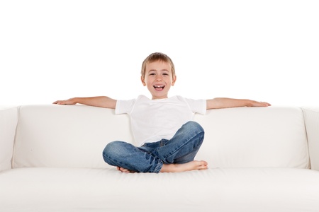 Happy young boy relaxing on sofa, settee or couch; white studio background.の写真素材