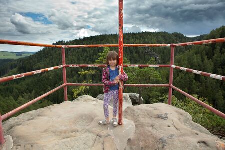 Girl standing on top of large rock, with safety railing, smiling and  holding a vertical post. の写真素材