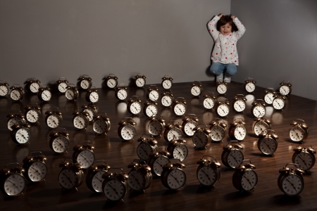 A girl in the corner of a room in which the floor is covered by alarm clocks. の写真素材