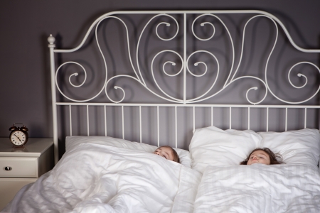 Sister and Brother sleeping in their parents bed with an alarm clock set. の写真素材