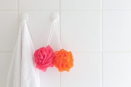 Tiled bathroom wall with towel on one hook and facecloth on another.の写真素材