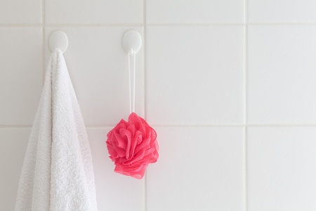 Tiled bathroom wall with towel on one hook and facecloth on another.の写真素材