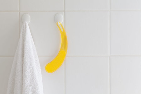 White towel and yellow file hanging on hooks on a white tile bathroom wall.