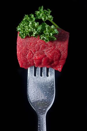 Piece of meat on a fork isolated on black backgrouの写真素材