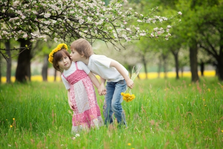 Two young children kissing in flowery meadow of long grass, girl wearing daisy flower crown.の写真素材