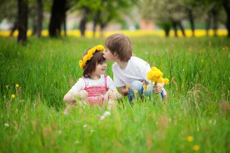 Two young children kissing in flowery meadow of long grass, girl wearing daisy flower crown.の写真素材
