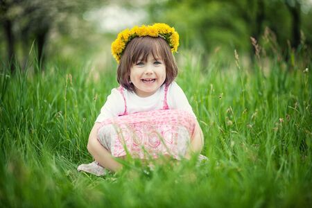 Young smiling girl sitting in tall green grass.の写真素材