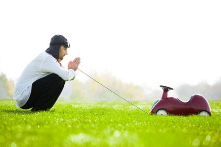 Man in retro style racing helmet with toy plastic car on green field.の写真素材