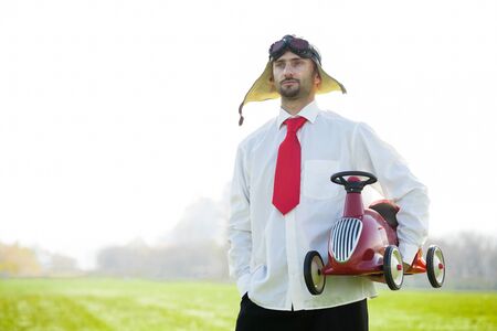 Adult race car driver holding a toy racing car wears a traditional leather helmet and goggles.の写真素材