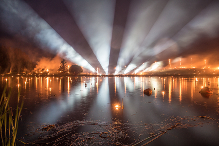 Searchlight show with fire show over a lake at nightの写真素材