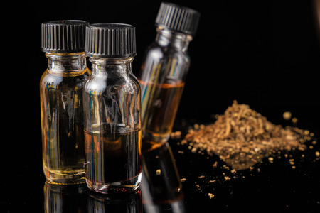 E-liquid bottles next to grinded tobacco leavesの写真素材