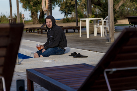 Student in a hoodie drinking beer and tipping legs into pool waterの写真素材