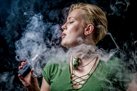 Young adult female exhaling smoke clouds from electronic cigaretteの写真素材