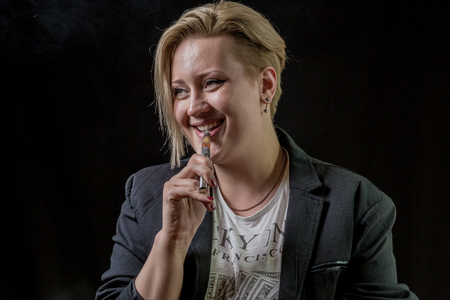 Happy and smiling woman holding electronic cigarette between her teethの写真素材