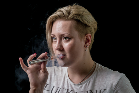 Young adult female exhaling smoke from electronic cigaretteの写真素材