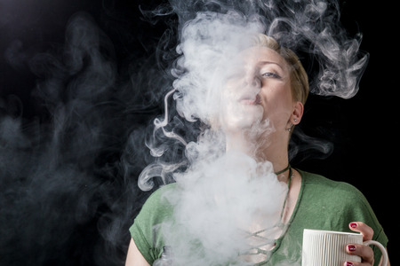 Young adult female exhaling smoke clouds from electronic cigaretteの写真素材