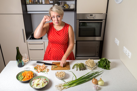 Female in kitchen cutting asparagus and rubbing her eyeの写真素材