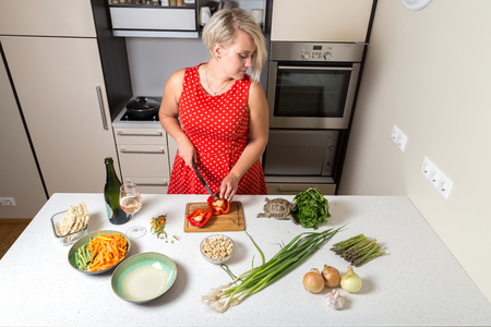 Woman cutting paprika and looking over shoulder of tortoise eating saladの写真素材
