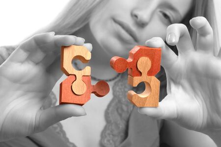 Young woman bringing together puzzle pieces. Monochrome gray background.