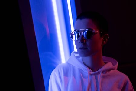 Colorful portrait of a young short haired woman wearing shiny sunglasses and standing in neon lights.の写真素材