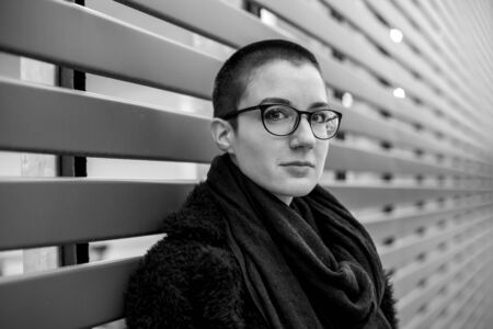 Emotional black and white portrait of a short haired young woman wearing glasses and an elegant black coat.の写真素材