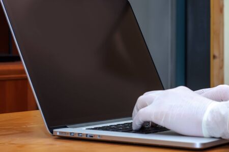 View on a doctors hands typing on a laptop PC while wearing medical gloves againts diseases like influenza or coronavirus.の写真素材