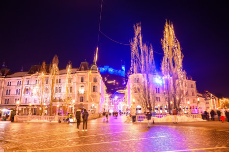 LJUBLJANA, SLOVENIA - JANUARY 15, 2022: View of the people walking on the Preseren Square and the Tromostovje Triple bridge with the Ljubljana Castle in the background during the Christmas holidays at nightのeditorial素材