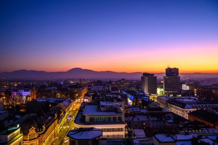 View on the city of Ljubljana from a skyscraper during sunset to night with the mountains in the background.のeditorial素材