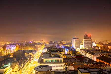 View on the city of Ljubljana from a skyscraper during sunset to night with the mountains in the background.のeditorial素材